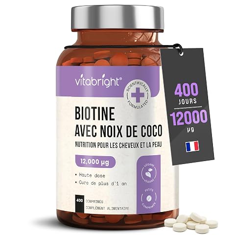 Flacon compact de biotine avec un micro-comprimé, posé sur une pierre claire dans une salle de bain
